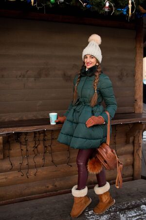 Beautiful smiling girl holding a cup of tea or coffee in winter. Beautiful woman in the winter on the street with New Year decorations. Christmas Fair.の写真素材