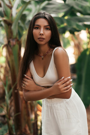 Portrait of a beautiful brunette in a tropical garden. A beautiful girl in white clothes on a background of banana palms.の写真素材