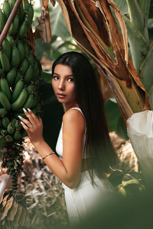 Portrait of a beautiful brunette in a tropical garden. A beautiful girl in white clothes on a background of banana palms.の写真素材