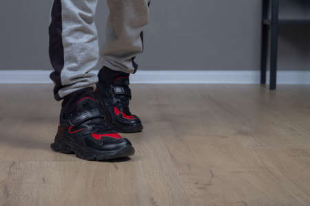 Black and red sports sneakers on the feet of a teenager at home on the floor.の写真素材