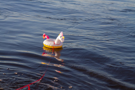 Inflatable circle a small unicorn floats on the water rainbow tied to a string, summer vacation at...