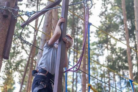 A boy overcomes obstacles in a rope park, a child with insurance and a protective helmet holds on to the ropes and passes over the abyss.の写真素材