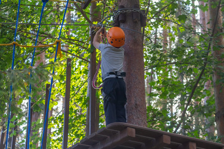 A boy overcomes obstacles in a rope park, a child with insurance and a protective helmet holds on to...