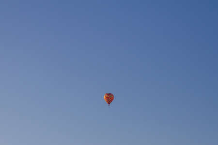 An orange balloon carries people balloonists tourists across the blue sky.の写真素材