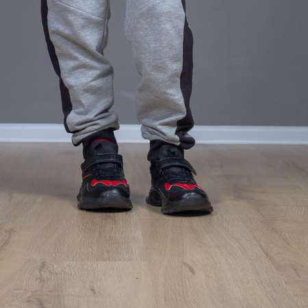 Sports shoes sneakers for a boy in black and red colors on the childs feet on the floorの写真素材