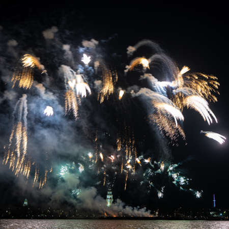 Festive fireworks in the dark sky with reflection in the water of the river at nightの写真素材