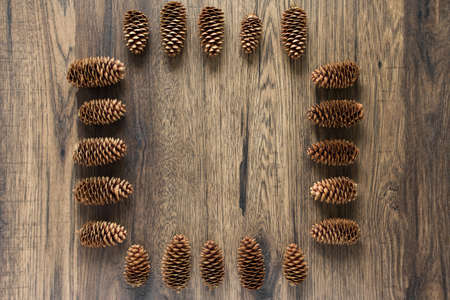 Christmas frame made of cones on a dark wooden background. Christmas, winter concept. Flat lay, top view.の写真素材
