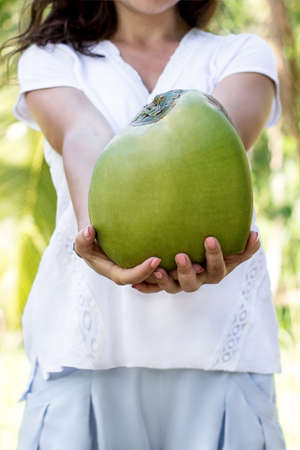 Girl in a white t-shirt holding a green coconutの写真素材