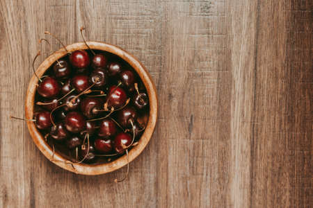 Ripe red cherries in a wooden cup on a wooden tableの写真素材