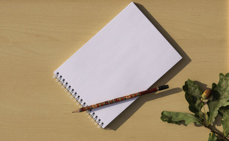 Notebook with a pencil on a wooden substrate with an oak branch with green leaves and an acorn