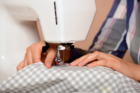 Close-up female hands sewing fabric on sewing machineの写真素材