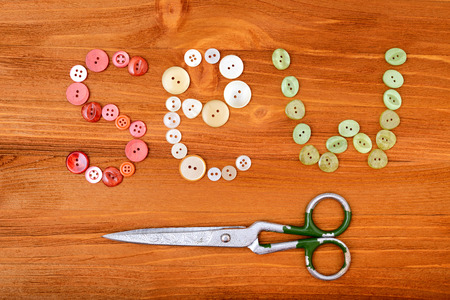 Word "sew" from multicolored sewing buttons and scissors on wooden backgroundの写真素材