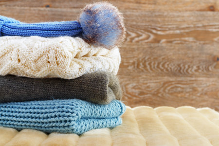 Warm clothing lies in a pile on a fluffy soft rug. Knitted sweaters on a wooden background. Autumn and winter conceptの写真素材