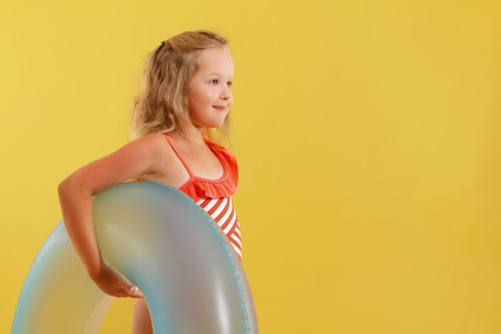 Little happy child  girl in a bathing suit holding an inflatable circle in his hands. Yellow background. The concept of leisure and travel.の写真素材