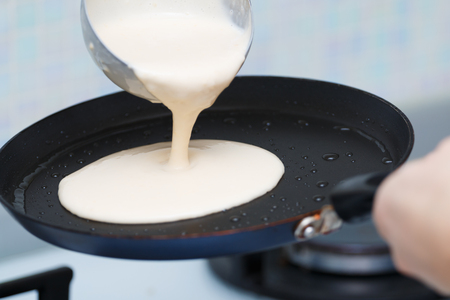 Closeup cooking pancakes on a gas stove. On a hot skillet liquid dough from the ladle is pouredの写真素材