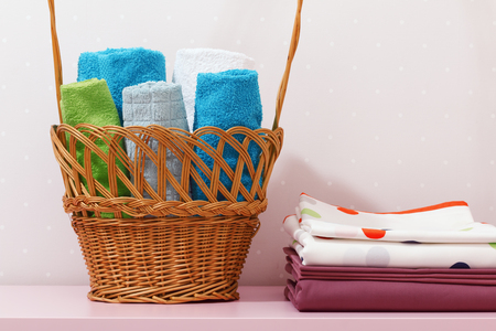 On the dresser there is a stack of clean ironed bed linen and there is a basket in rolls of folded multicolored towels.の写真素材