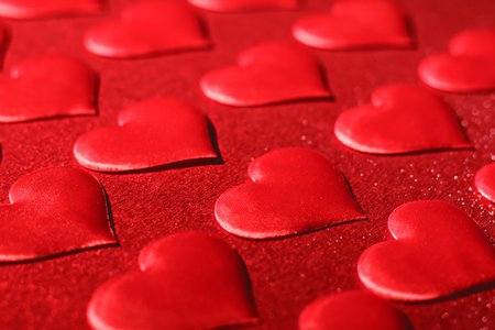 Closeup of a red heart on a shiny red background. The concept of love, choice and celebration of Valentine's Day. Selective focus.の写真素材