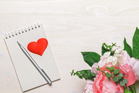 Opened blank notepad with spiral, gray pen, heart and pink peony flowers on white wooden background. Top view. Copy space.の写真素材