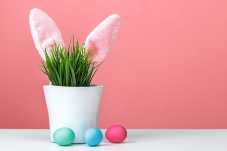 Rabbit ears sticking out of a flower pot with green grass, are multi-colored eggs. Easter concept....
