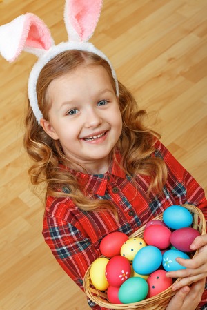 A cute little child girl with bunny ears sits on the floor with a basket of Easter eggs.の写真素材