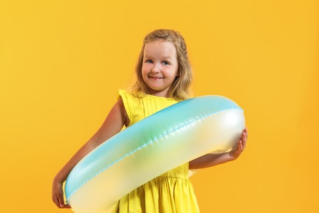 Portrait of a happy child little girl in a dress with a swimming ring on a colored yellow background. Vacation conceptの写真素材