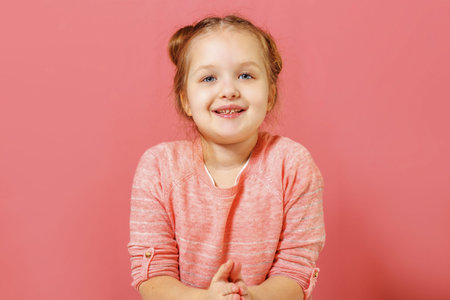 Closeup portrait of cute little child girl with buns of hair over pink background