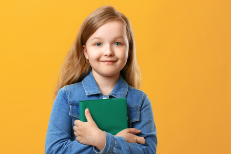 The little girl the student in a denim shirt on a yellow background. The child holds a book. The concept of education and school.の写真素材