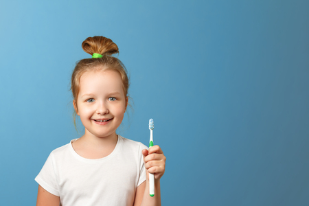 Closeup portrait of a little girl on a blue background. A child holds a toothbrush. The concept of daily hygiene. Copy space.の写真素材