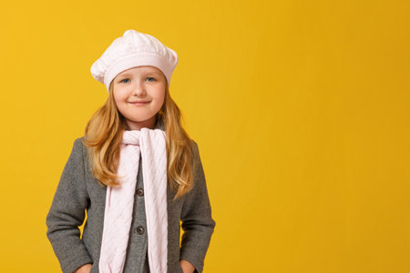 Portrait of a cheerful child in a gray coat and beret on a yellow background. Little girl blonde looks into the camera. Autumn concept. Copy spaceの写真素材