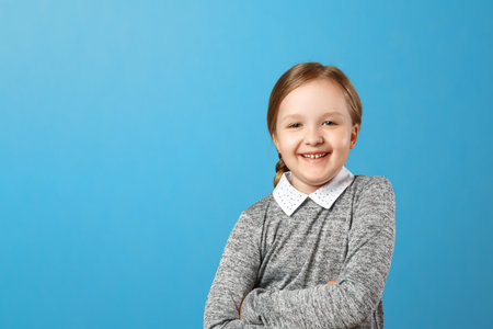 Portrait of a cheerful little girl on a blue background. Child schoolgirl laughs and looks into the...