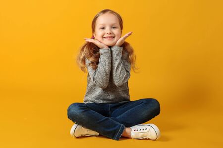 Portrait of a beautiful cute attractive charming cheerful little girl. The child sits on a yellow background in the studio.の写真素材