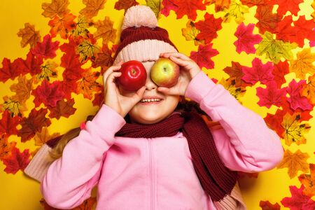 Top view of a happy little girl lying on autumn leaves. A child in a scarf and hat.の写真素材