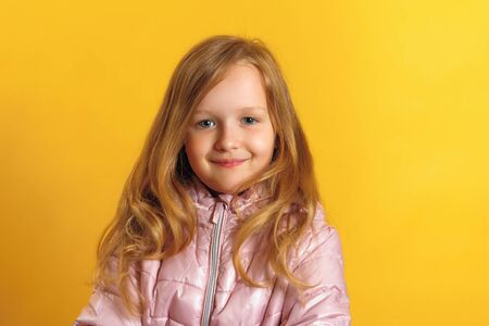 Portrait of a cute little girl in a jacket on a yellow background. Autumn and winter concept.の写真素材