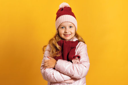 Portrait of a cute little girl in a jacket, scarf and hat on a yellow background. Autumn and winter concept.の写真素材