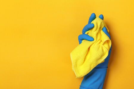 A hand in a protective blue glove holds a yellow rag on a yellow colored background.の写真素材