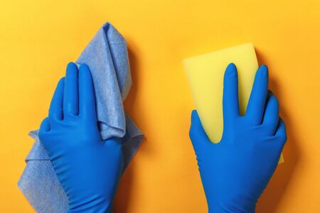 Hands in protective blue gloves hold a sponge and a napkin on a yellow colored background.の写真素材