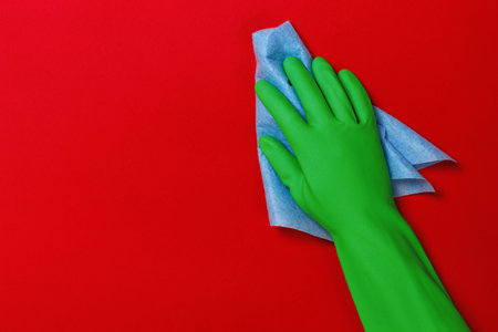 Worker's hand in a protective green glove with a blue rag on a red background. Cleaning concept.