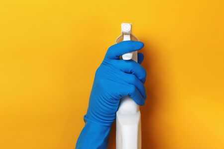 A hand in a protective latex glove holds a spray bottle on a yellow colored background.の写真素材