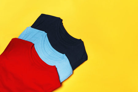 Top view of a composition with multi-colored t-shirts on a yellow background. Copy space.