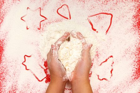 Children bake cookies for Christmas. Hands, star, tree, bell, heart, flour on a red background. Top view.の写真素材