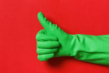 Thumb up in a protective glove of green color on a red background.の写真素材