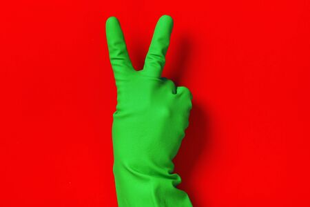 Victory sign in a protective glove of green color on a red background. Success concept.の写真素材