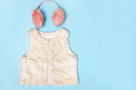 A set of warm clothes. Fluffy pink earmuffs and a white vest on a blue background. Top view flat lay copy space.の写真素材