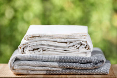 A stack of folded bedding. Monochrome gray white gradient plaid bed sheet textile set on blurred foliage background.の写真素材