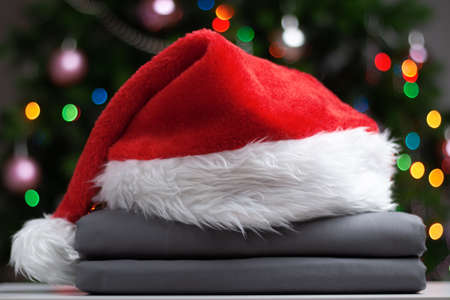 A stack of folded bedsheets with a Santa hat against the backdrop of a Christmas tree with lights.の写真素材