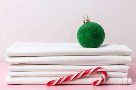 A stack of clean white sheets, a Christmas tree ball, and a candy cane.の写真素材
