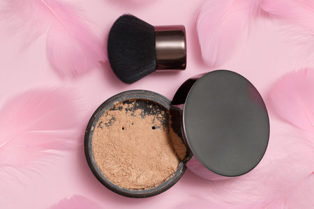 Cosmetic loose powder for face makeup in an open jar with a brush on a pink background.