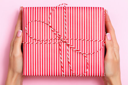 Close-up of female hands holding a large red and white striped gift box on a pink pastel background. Birthday valentine's day new year christmas.の写真素材