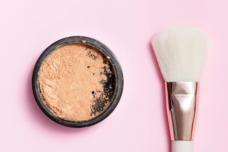 Cosmetic loose powder for face makeup in an open jar with a face brush on a pink background.の写真素材
