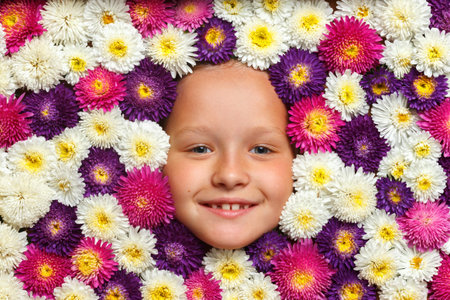 Cheerful cute face of a little girl in flowers aster colors of white, purple, pink. Top view of the...